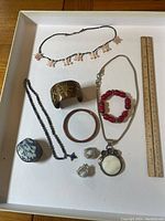 Full lot image with all jewelry pieces arranged on a white tray with wooden floor background. Includes various necklaces, earrings, bracelets and rings.