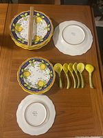 Overall view of six lemon patterned plates stacked with six yellow spoons and one single plate back showing 'MOD DERUTA ITALY' mark