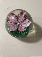 View of Murano glass paperweight showing detailed purple flower and green textured base inside clear glass sphere.