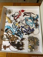 Photo showing assorted necklaces and pendants in tray including various bead colors and cross pendants.