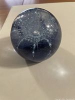 Photo showing the deep blue spherical paperweight with internal bubbles and liquid-like teardrop formations inside the glass.