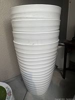 Four stacked white plastic planters with horizontal ribbed pattern, light wear visible, standing against a wall indoors.