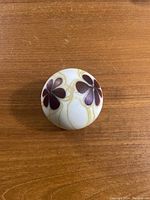 Top view showing round white glass paperweight with three red flower motifs and cream swirls on wooden surface.