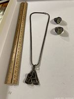 Necklace with initial shaped pendants B, A, M beside ruler for size reference, and two silver rings with green stones.