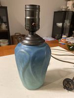 Blue Van Briggle art pottery lamp base shown from a front side angle with metal socket and attached cord with vintage plug visible.