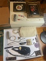 Two framed floral artworks, assorted vintage costume jewelry including bracelets, brooches, and crochet purses displayed on white surface