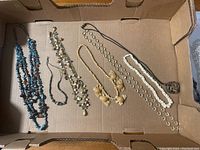 Top-down photo of six necklaces in a cardboard box, showcasing variety of bead colors and styles.