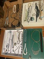 Top view of four trays containing various vintage necklaces with different styles and materials.