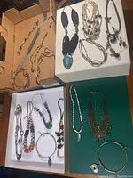 Wide view of vintage necklaces displayed on three trays and a green surface, showing metals, beads, pendants, and pearl strands.