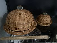Side-by-side photo of large and small rattan domed serving trays with glass knobs and ruler for scale