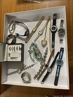 Overview of watch lot displaying multi-style wristwatches and watch accessories in a tray.
