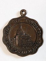 Front view of bronze-colored pendant featuring City Hall embossed design and inscriptions commemorating Kingston restoration in 1973.