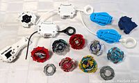 Top-down view of multiple Beyblade spinning tops and launchers including ripcords arranged on a white surface.