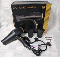 Bio Ionic Gold Pro 24K Gold hair dryer with box, two nozzle attachments, power cord and adapter, and user manual laid out on white background.