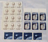 Block of 15 St. Laurent 7 cent Canadian stamps, strip of 4 Alouette 5 cent stamps, and block of 6 Christmas candles 8 cent stamps on white surface.