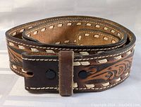 Rolled western tooled brown cowhide leather belt showing detailed tooling and stitched edges.