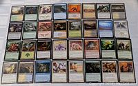 Top-down view of 32 Magic the Gathering cards arranged in four rows of eight cards each. Cards display various illustrations including creatures, spells, and landscapes.