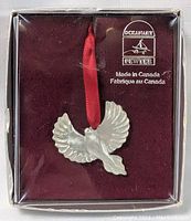 Front view of silver-colored pewter bird ornament in original packaging with Ocean Art logo, Made in Canada label, and red hanging ribbon visible.
