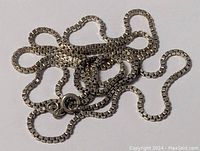 Close-up image of the sterling silver necklace chain laid out, showing the box link chain and spring ring clasp.