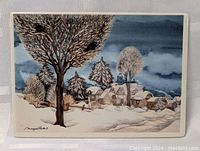 Porcelain card front showing winter village with snow-covered trees and houses under cloudy sky, signed by artist.