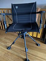 Front angled view showing the black fabric chair with white piping, padded armrests and the sturdy four-leg metal frame with swivel feet.