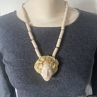 Necklace being worn on a mannequin showing the full length and central figural pendant detail.