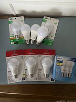 Nine LED lightbulbs laid out on surface showing unopened packages and loose bulbs, some marked 60W and others 100W.