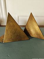 Pair of brass pyramid-shaped bookends showing hexagonal pattern on front sides.