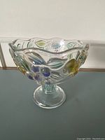 Front and side view of the clear glass pedestal bowl with colorful embossed fruit and leaf designs on the bowl surface.