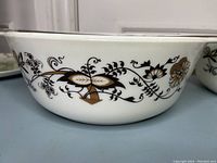Close-up side angle of one Pyrex casserole dish showing brown grapevine floral motif around the white glass bowl-shaped dish.
