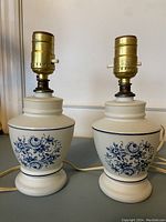 Pair of vintage blue and white floral pattern bedside lamps showing floral designs on ceramic bases and brass light sockets.