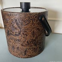 Side view of vintage Irvinware ice bucket showing tooled faux leather with floral scroll leaf emboss pattern and black handle.