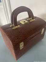 Closed view of brown embossed travel case with handle and brass lock/latches