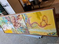 Full view of the triptych painting laid on the floor showing the entire artwork and frame.