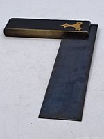 Full view of antique carpenter's angle square showing steel blade and brass handle with brass inlay detail.