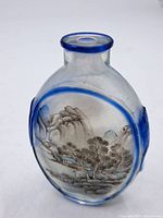 Front view of oval snuff bottle with painted landscape scene and blue glass rim.