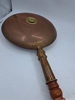 Full view of the copper pan with brass lid and wooden handle attached, showing the overall shape and size.