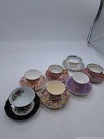 Seven assorted vintage teacups and saucers displayed in a group, showing variety in pattern, color and style.