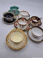 Group photo showing seven assorted vintage teacups and saucers with varied patterns and gold accents.
