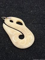 Front view of the carved bone pendant showing stylized hook shape and carved details