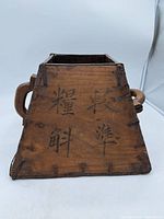 Front and side view of wooden container with Chinese characters and handle visible.