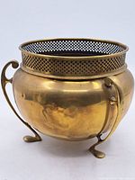 Front angled view of the small brass footed jardiniere, showing the curved handles, round body, and lattice rim detail.