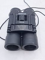 Front view of black Tasco 10x25 binoculars showing both eyepieces and neck strap inlet.
