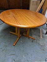 Full view of round teak tabletop and twin pedestal base on concrete floor