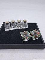 Front view of three salt and pepper shakers, two clear cut-glass and one painted glass, all with sterling silver lids on black background.