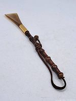 Full view of the vintage shoehorn with brass scoop and bamboo-style handle with leather strap.