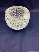 Clear and white striped Murano glass ashtray bowl with cigarette rests on the rim, shown against a dark background.