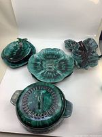 Photo showing four pottery serving pieces including two leaf-shaped plates, a flower-shaped plate, and a lidded casserole dish with handles in signature Blue Mountain Pottery green and black glaze.