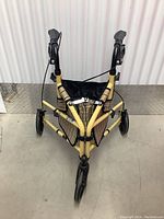 Top-down view of folded yellow metal walker with three wheels and plaid fabric basket attached.