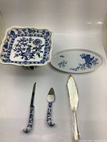 Lot of blue and white dishes including cake stand, oval dish, and three serving utensils with porcelain handles.